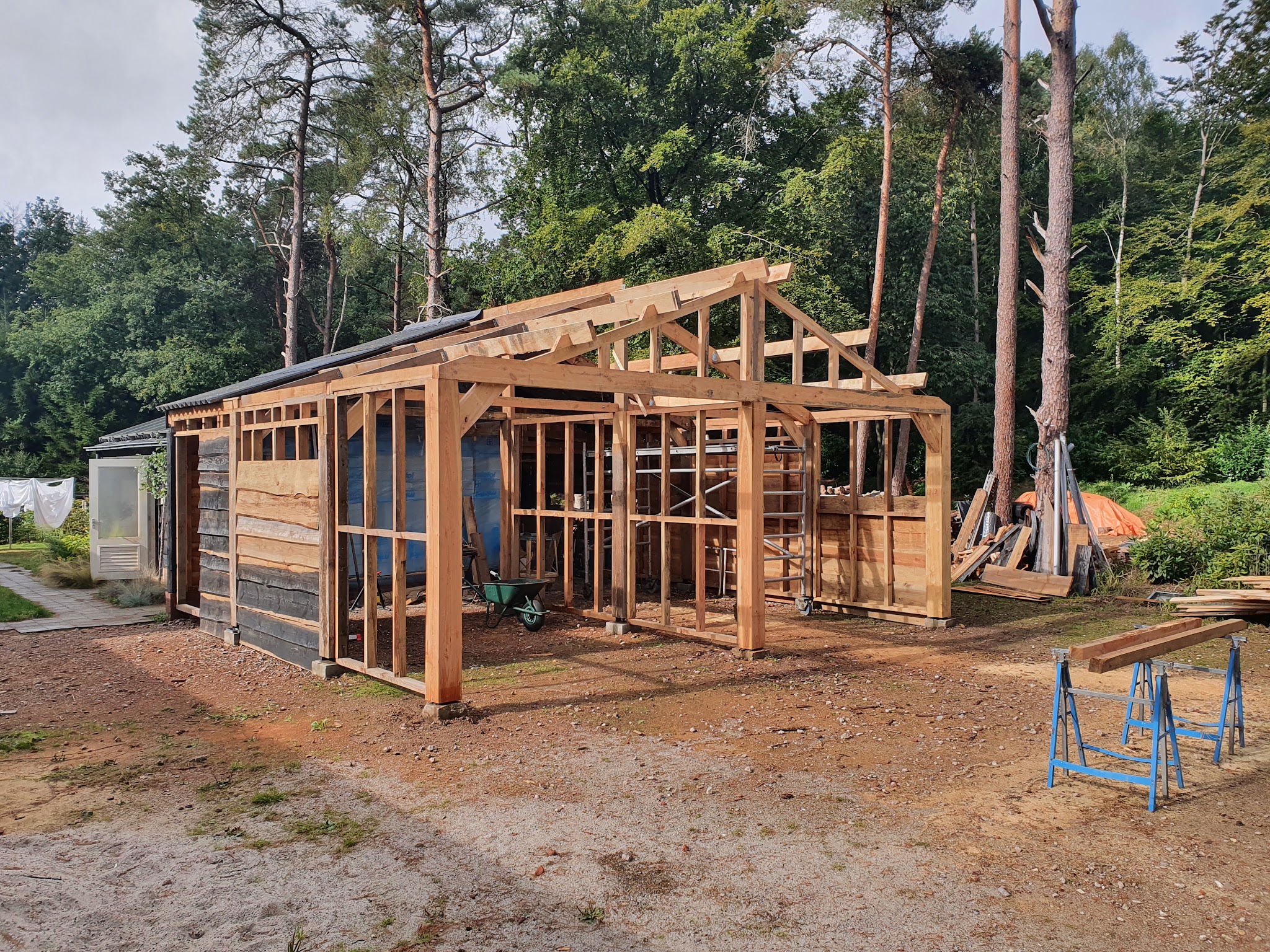 Houten bijgebouw in aanbouw, spanten en regelwerk nog open, schragen op de voorgrond