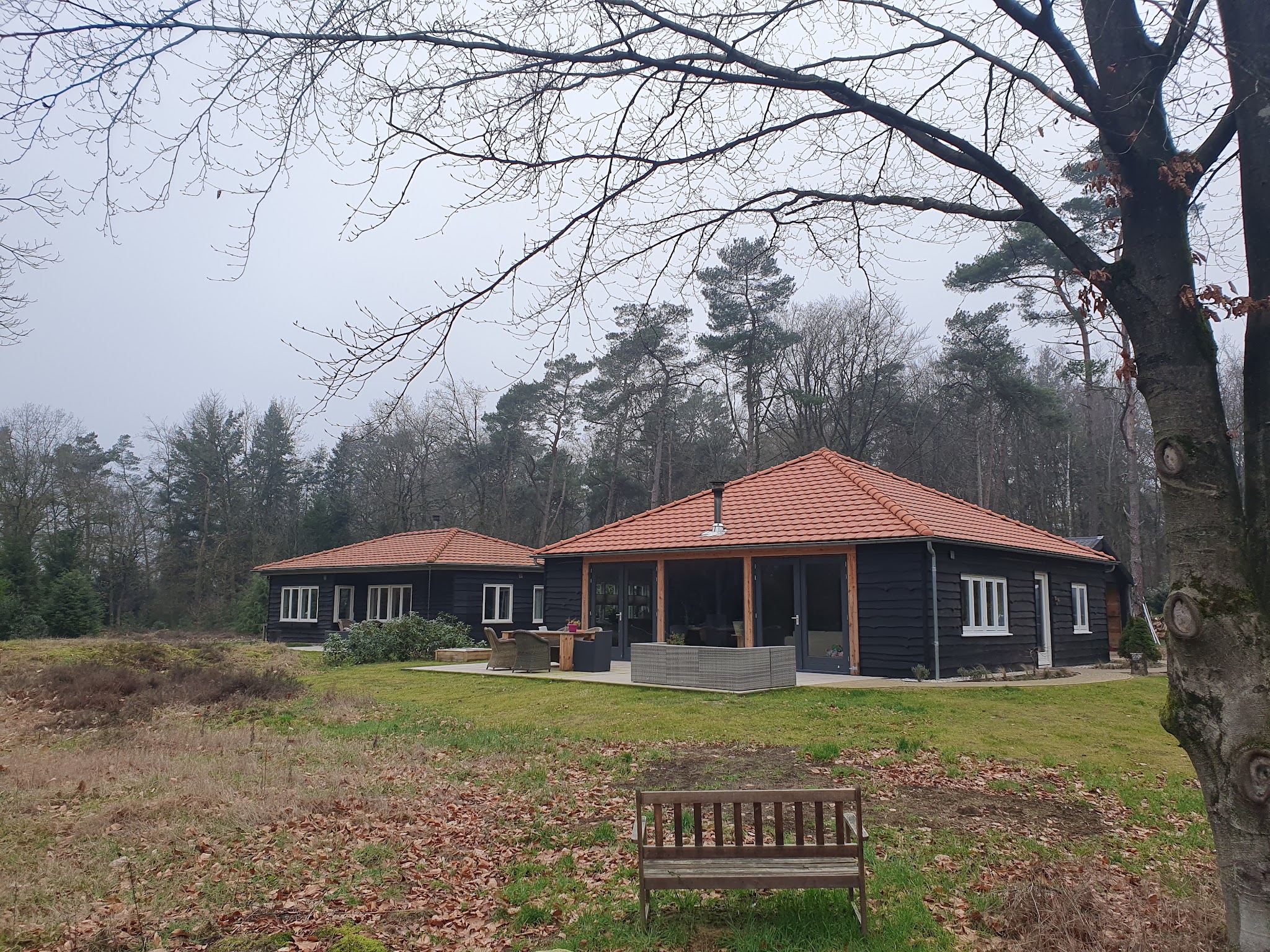 Afgewerkt zwart houten huis met terracotta pannendaken, midden in het bos