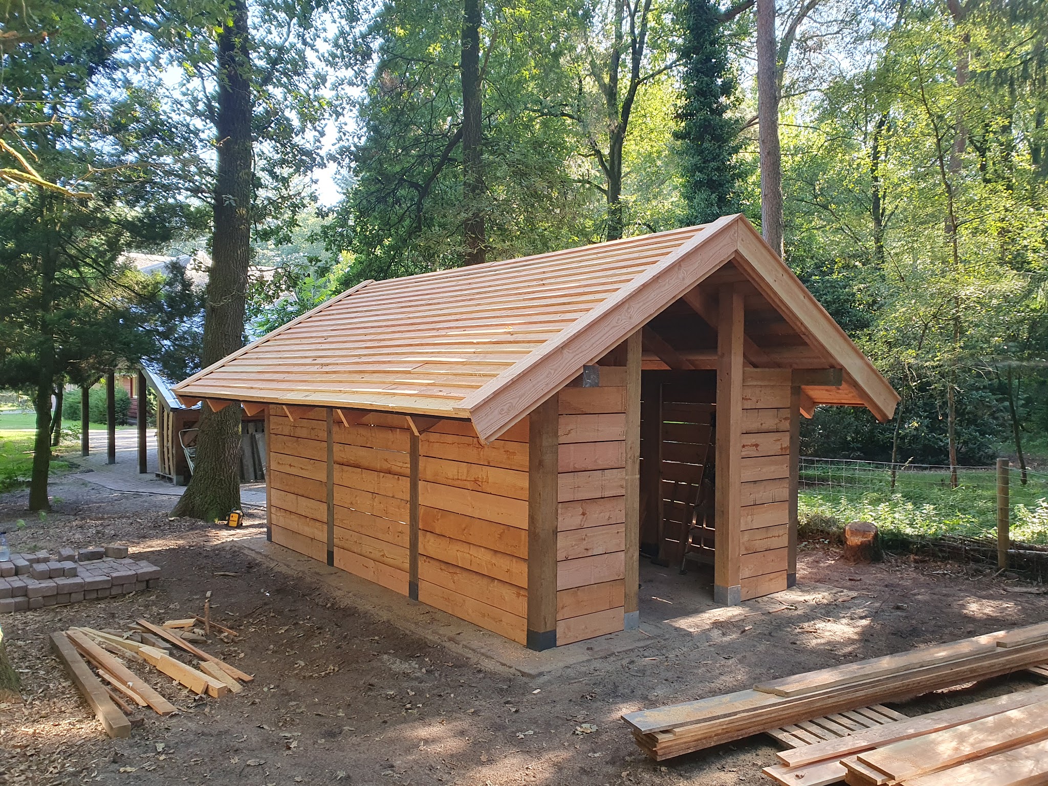 Nieuw houten bijgebouw met lariks gevelbekleding en een geschaald dak, net opgeleverd tussen de bomen