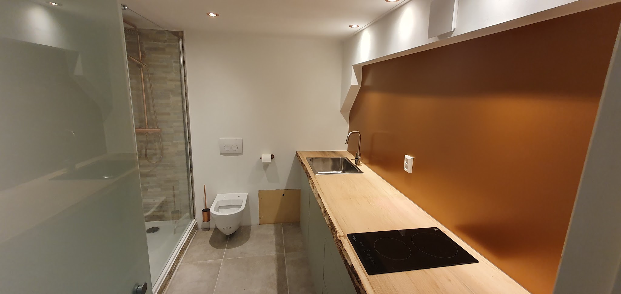 Afgewerkte doucheruimte met keukenblok, natuursteen in de douche en een houten blad met boomstamrand